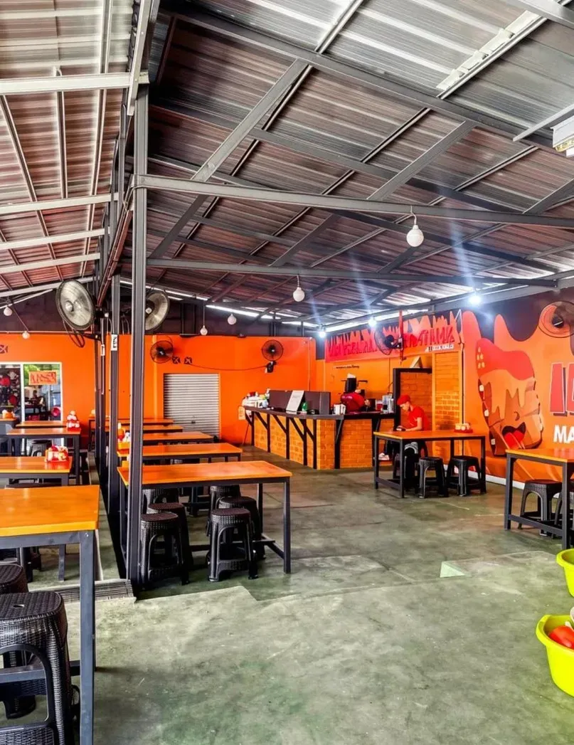 Area makan beratap tinggi dengan meja oranye dan bangku hitam